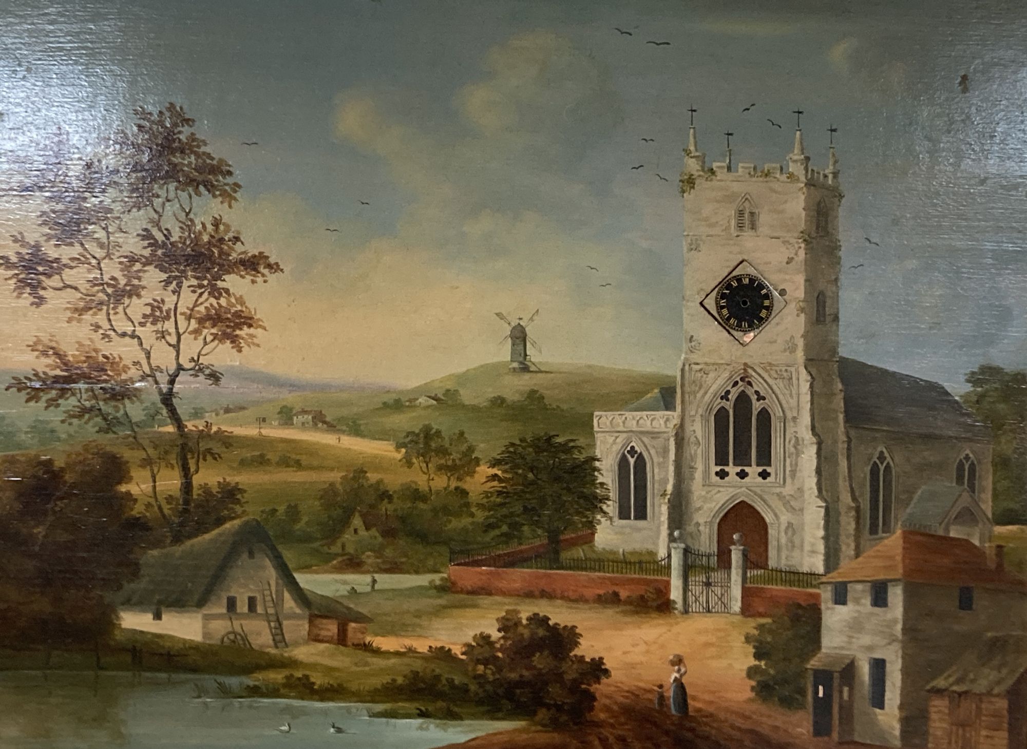 Victorian School, oil on wooden panel, Landscape with church and windmill inset with a watch dial, but movement now lacking, 41 x 56cm